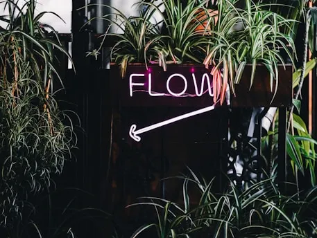 a neon sign that reads flow next to some plants