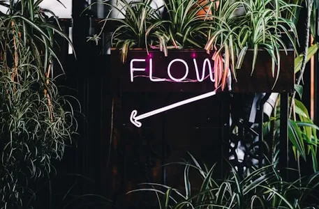 a neon sign that reads flow next to some plants
